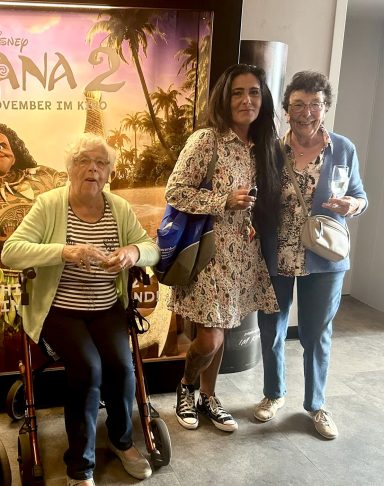 Drei Frauen posieren vor einem "Moana 2"-Plakat. Eine sitzt, die anderen stehen daneben.